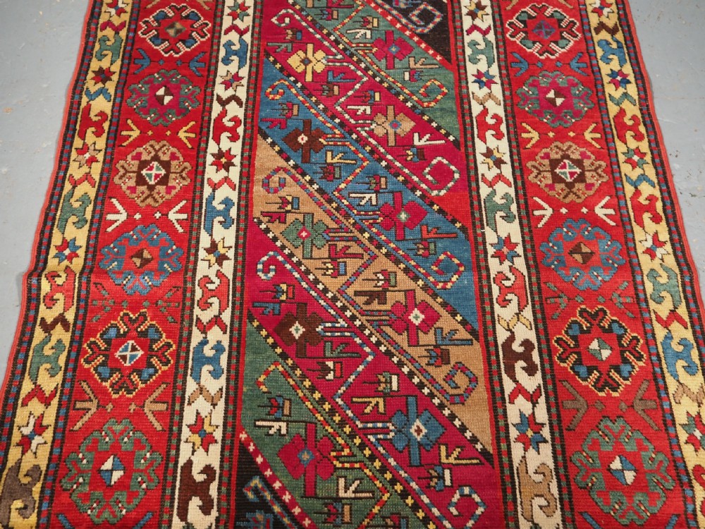 An antique Caucasian Gendje Kazak hand-knotted wool rug featuring diagonal polychrome stripes within a wide geometric border on a red field. View III