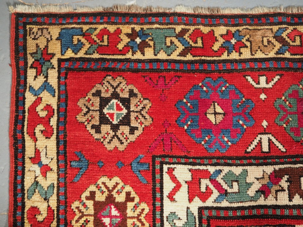 An antique Caucasian Gendje Kazak hand-knotted wool rug featuring diagonal polychrome stripes within a wide geometric border on a red field. View V