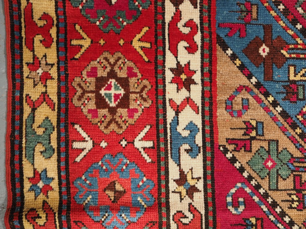 An antique Caucasian Gendje Kazak hand-knotted wool rug featuring diagonal polychrome stripes within a wide geometric border on a red field. View VI