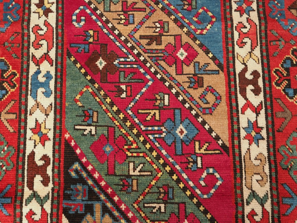 An antique Caucasian Gendje Kazak hand-knotted wool rug featuring diagonal polychrome stripes within a wide geometric border on a red field. View VIII