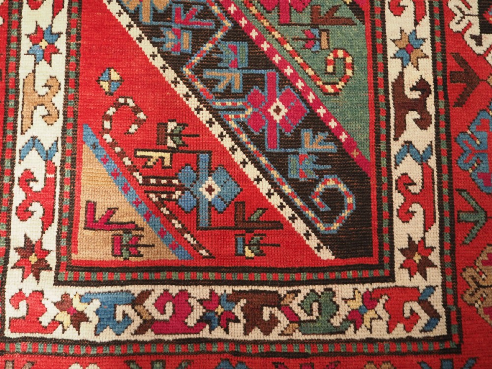 An antique Caucasian Gendje Kazak hand-knotted wool rug featuring diagonal polychrome stripes within a wide geometric border on a red field. View IX