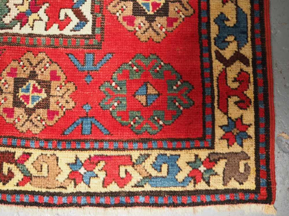 An antique Caucasian Gendje Kazak hand-knotted wool rug featuring diagonal polychrome stripes within a wide geometric border on a red field. View X