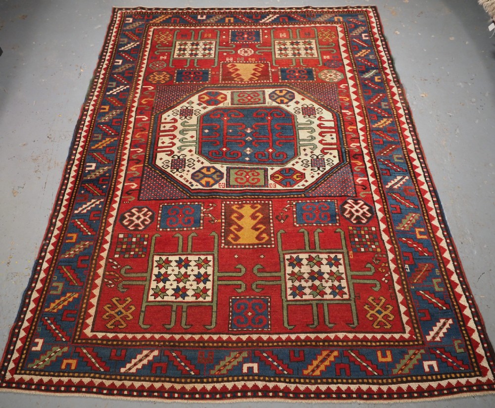 An antique hand-knotted Caucasian Karachov Kazak wool rug featuring a red field with a large central octagonal medallion and blue geometric borders.