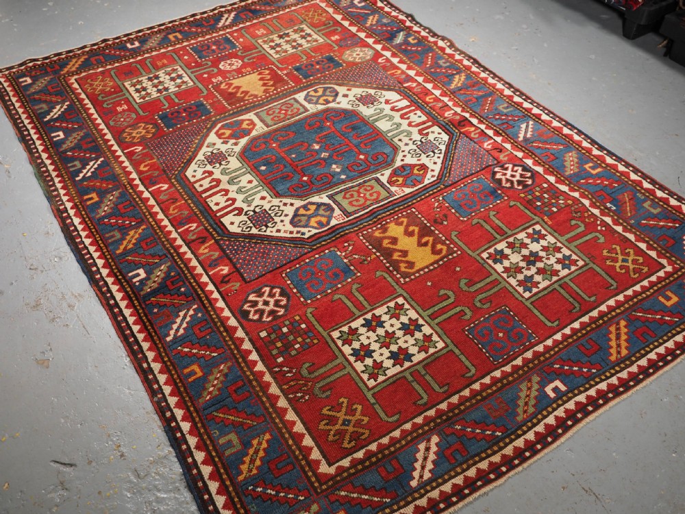 An antique hand-knotted Caucasian Karachov Kazak wool rug featuring a red field with a large central octagonal medallion and blue geometric borders. View II