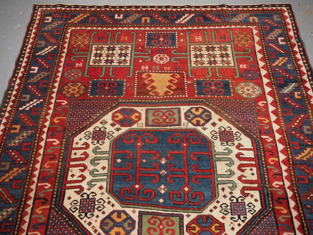 An antique hand-knotted Caucasian Karachov Kazak wool rug featuring a red field with a large central octagonal medallion and blue geometric borders. View III