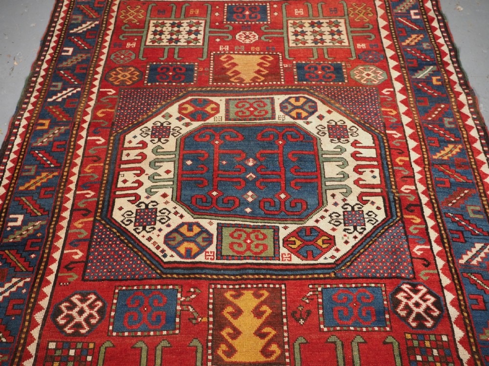 An antique hand-knotted Caucasian Karachov Kazak wool rug featuring a red field with a large central octagonal medallion and blue geometric borders. View IV