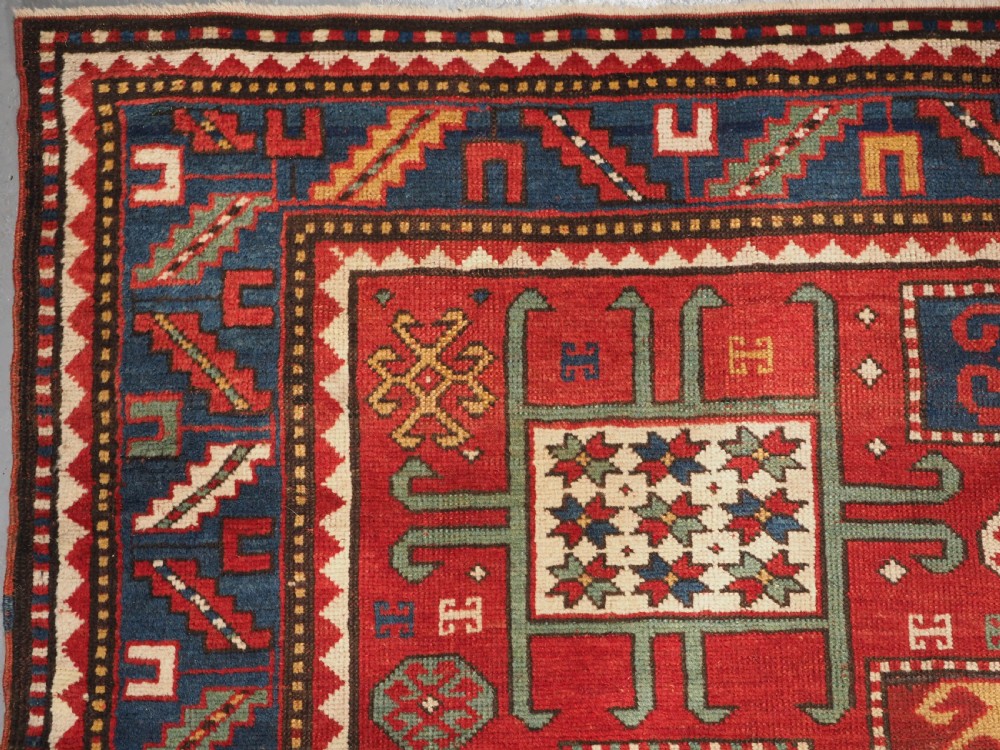 An antique hand-knotted Caucasian Karachov Kazak wool rug featuring a red field with a large central octagonal medallion and blue geometric borders. View V