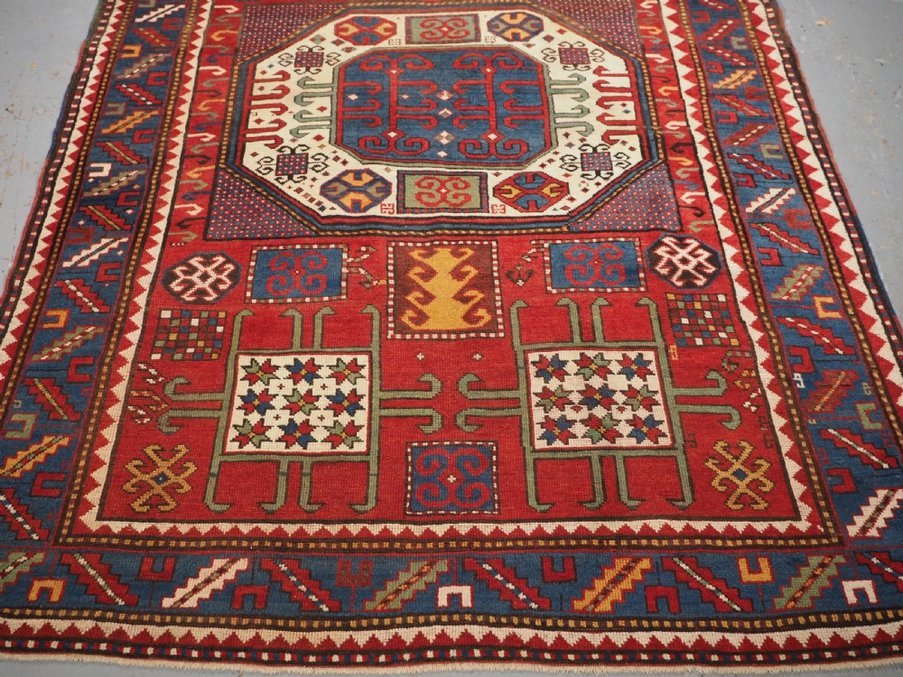 An antique hand-knotted Caucasian Karachov Kazak wool rug featuring a red field with a large central octagonal medallion and blue geometric borders. View VI