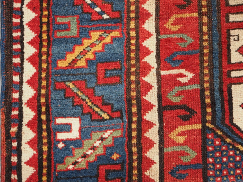 An antique hand-knotted Caucasian Karachov Kazak wool rug featuring a red field with a large central octagonal medallion and blue geometric borders. View VII