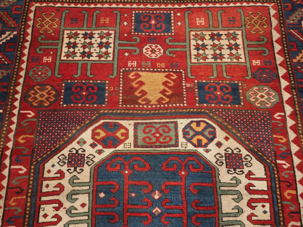 An antique hand-knotted Caucasian Karachov Kazak wool rug featuring a red field with a large central octagonal medallion and blue geometric borders. View VIII