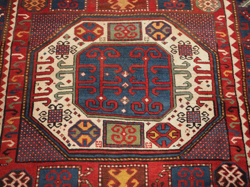 An antique hand-knotted Caucasian Karachov Kazak wool rug featuring a red field with a large central octagonal medallion and blue geometric borders. View IX