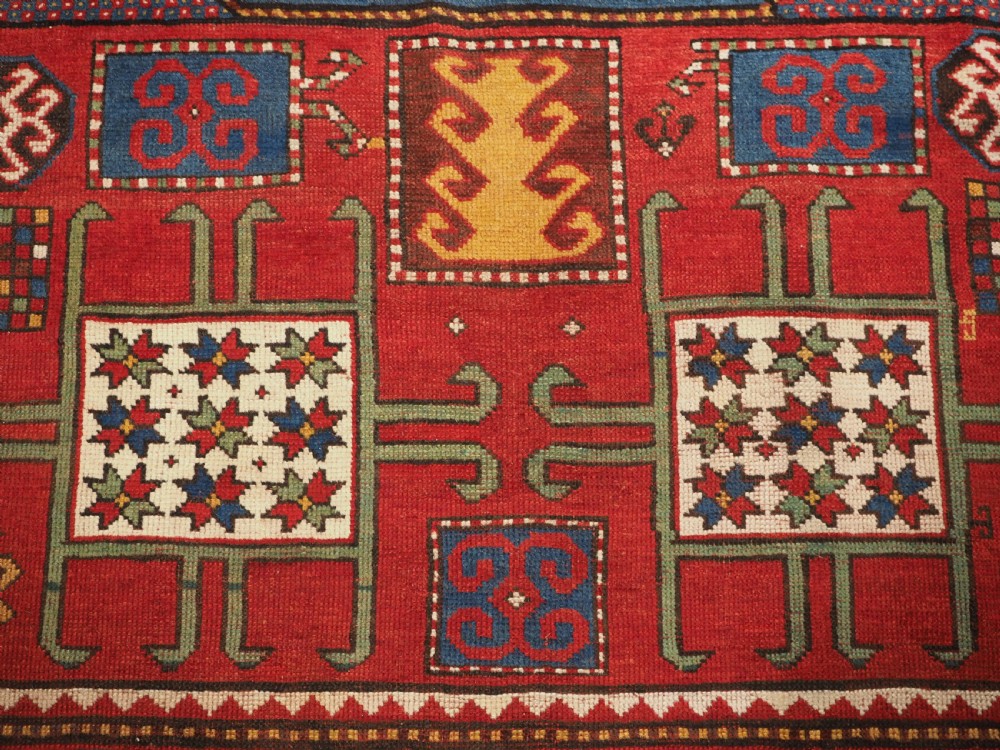 An antique hand-knotted Caucasian Karachov Kazak wool rug featuring a red field with a large central octagonal medallion and blue geometric borders. View X