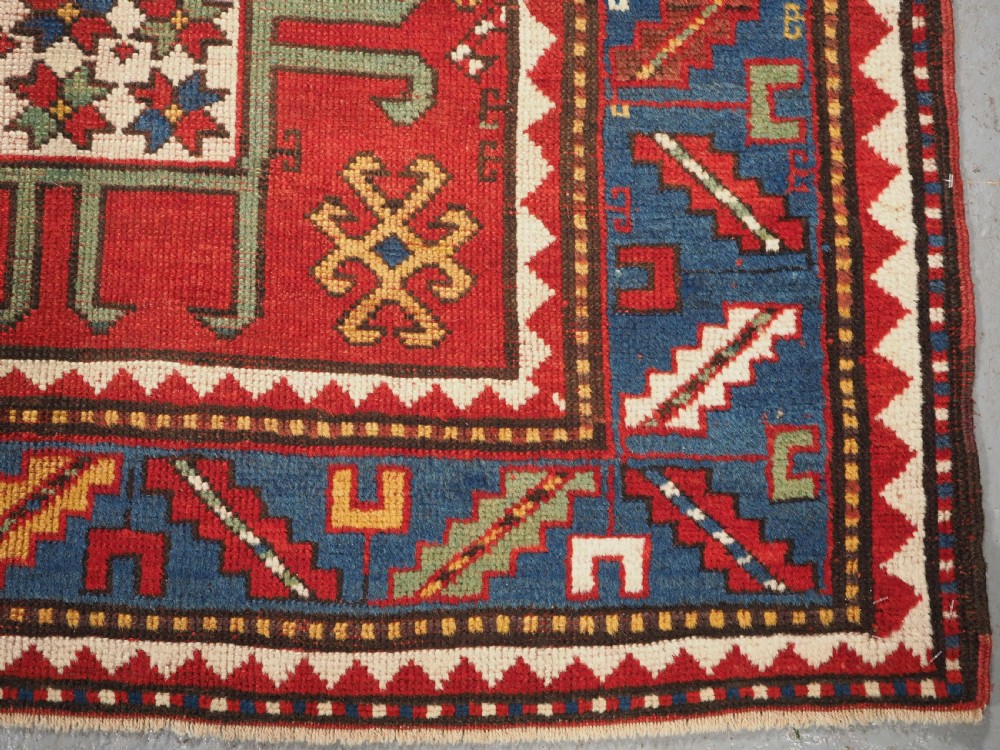 An antique hand-knotted Caucasian Karachov Kazak wool rug featuring a red field with a large central octagonal medallion and blue geometric borders. View XI