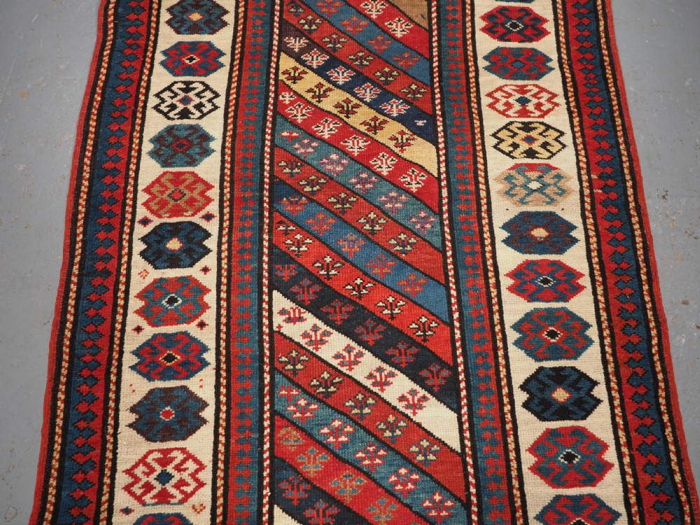 An antique Caucasian Gendje wool runner rug featuring a central field with diagonal stripes in red, blue, and cream surrounded by geometric borders. View III