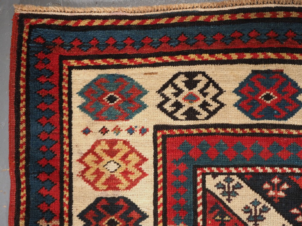 An antique Caucasian Gendje wool runner rug featuring a central field with diagonal stripes in red, blue, and cream surrounded by geometric borders. View VI
