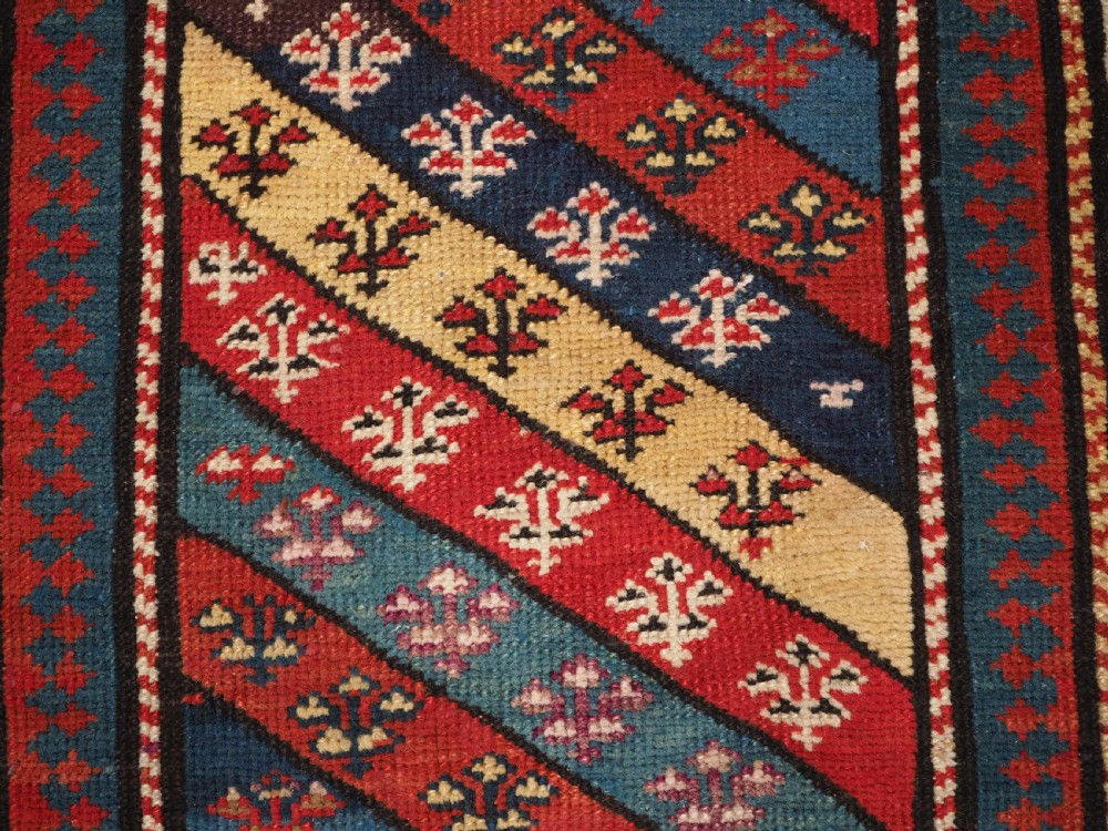 An antique Caucasian Gendje wool runner rug featuring a central field with diagonal stripes in red, blue, and cream surrounded by geometric borders. View VIII