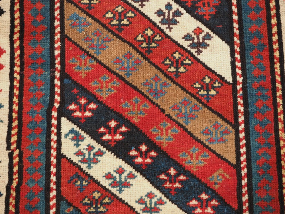 An antique Caucasian Gendje wool runner rug featuring a central field with diagonal stripes in red, blue, and cream surrounded by geometric borders. View X