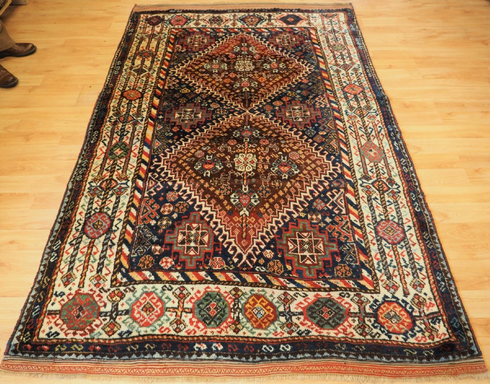 An antique Persian Qashqai Shekarlu wool rug featuring geometric diamond medallions in deep red, navy blue, and cream shades.