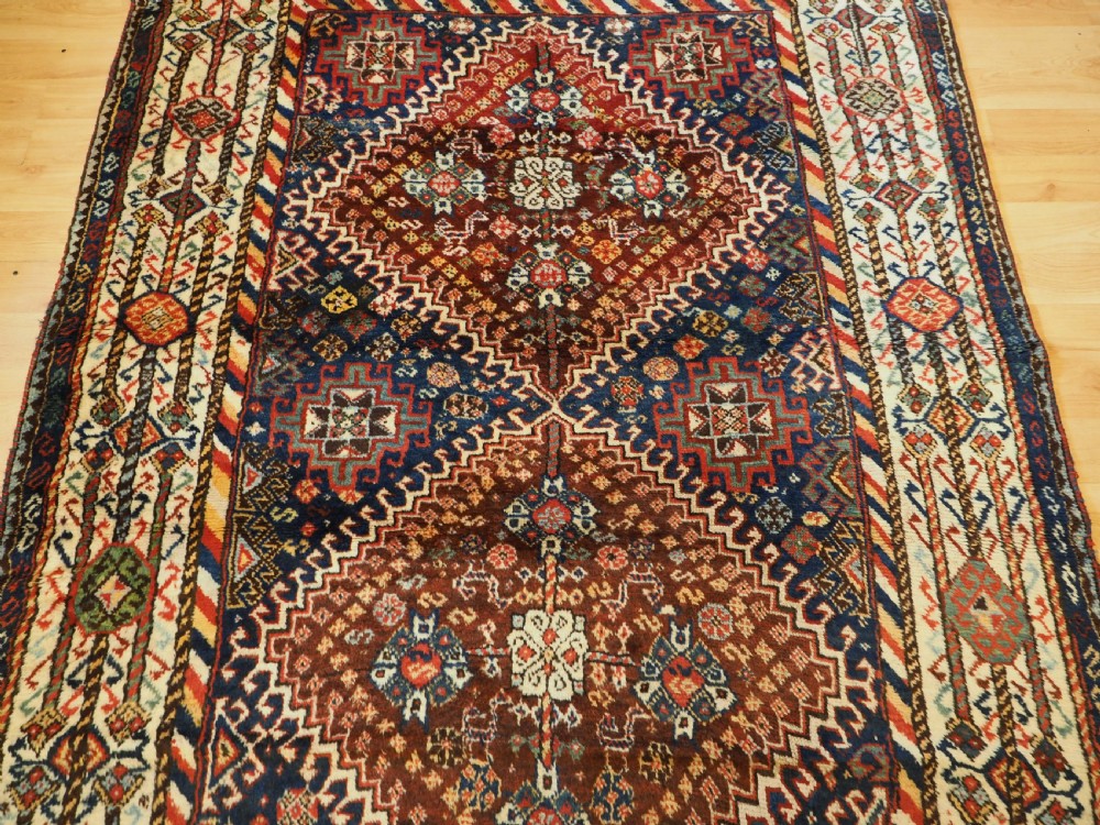 An antique Persian Qashqai Shekarlu wool rug featuring geometric diamond medallions in deep red, navy blue, and cream shades. View IV