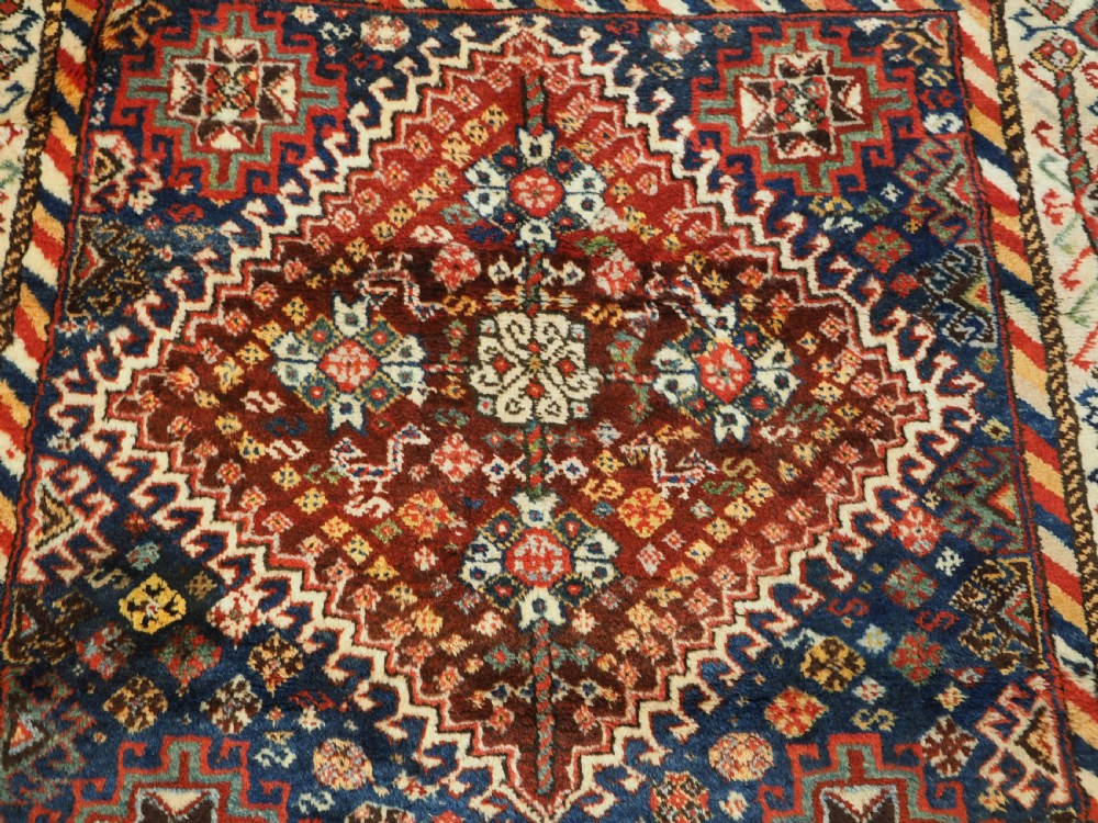 An antique Persian Qashqai Shekarlu wool rug featuring geometric diamond medallions in deep red, navy blue, and cream shades. View IX