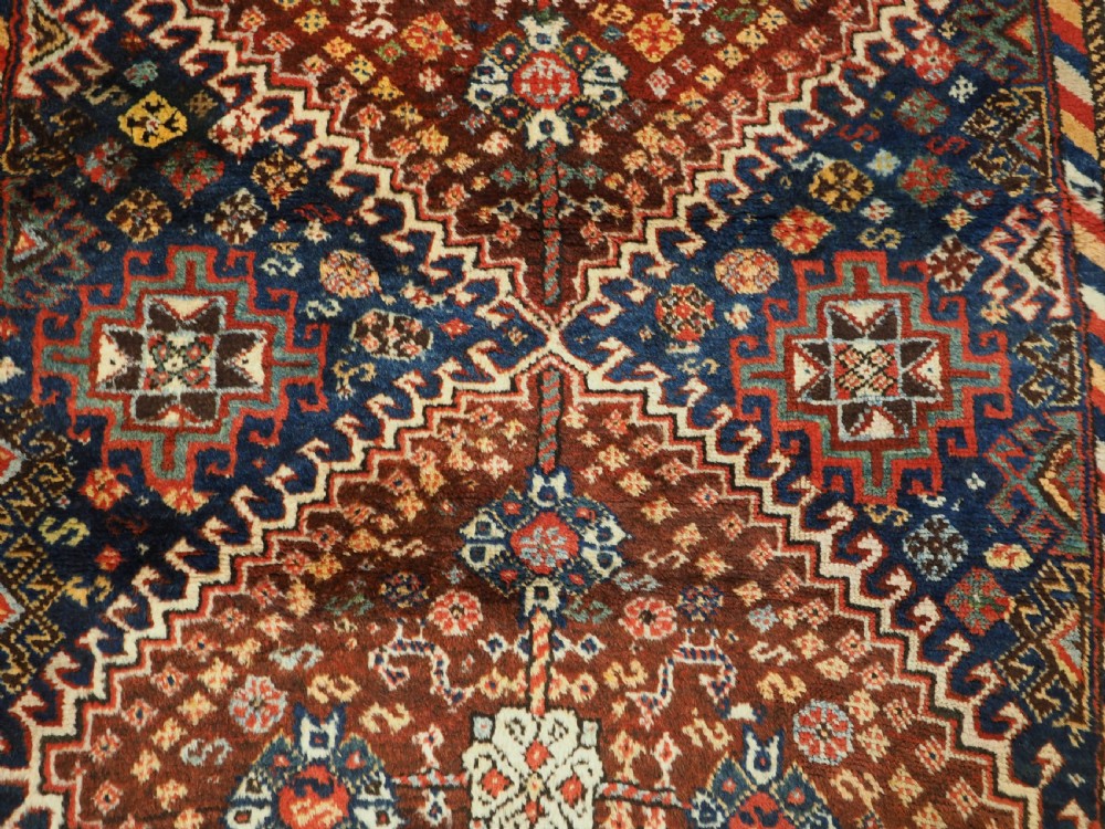 An antique Persian Qashqai Shekarlu wool rug featuring geometric diamond medallions in deep red, navy blue, and cream shades. View X