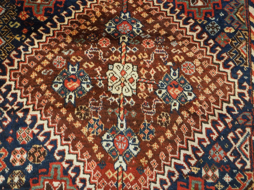 An antique Persian Qashqai Shekarlu wool rug featuring geometric diamond medallions in deep red, navy blue, and cream shades. View XI