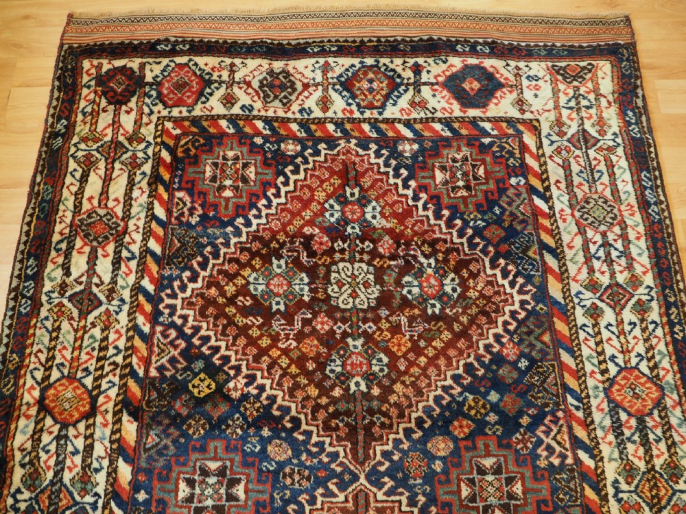 An antique Persian Qashqai Shekarlu wool rug featuring geometric diamond medallions in deep red, navy blue, and cream shades. View XII