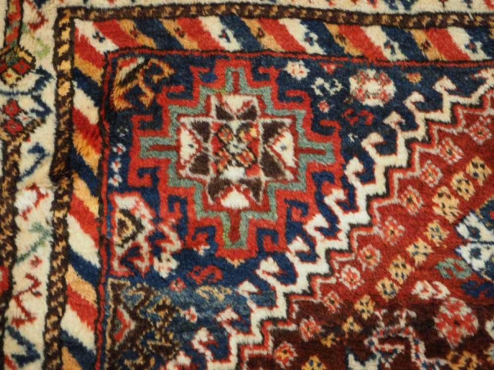 An antique Persian Qashqai Shekarlu wool rug featuring geometric diamond medallions in deep red, navy blue, and cream shades. View XVII