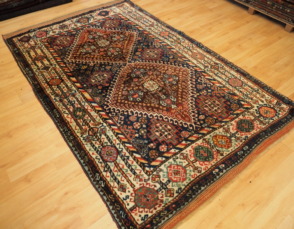 An antique Persian Qashqai Shekarlu wool rug featuring geometric diamond medallions in deep red, navy blue, and cream shades. View XIX