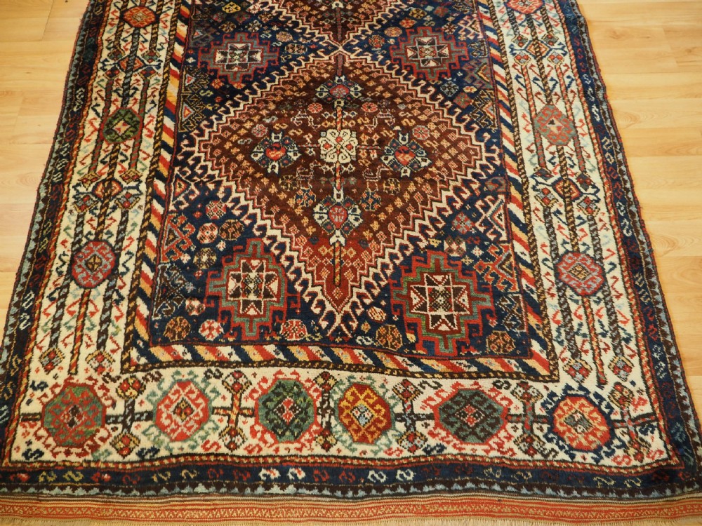 An antique Persian Qashqai Shekarlu wool rug featuring geometric diamond medallions in deep red, navy blue, and cream shades. View XXII