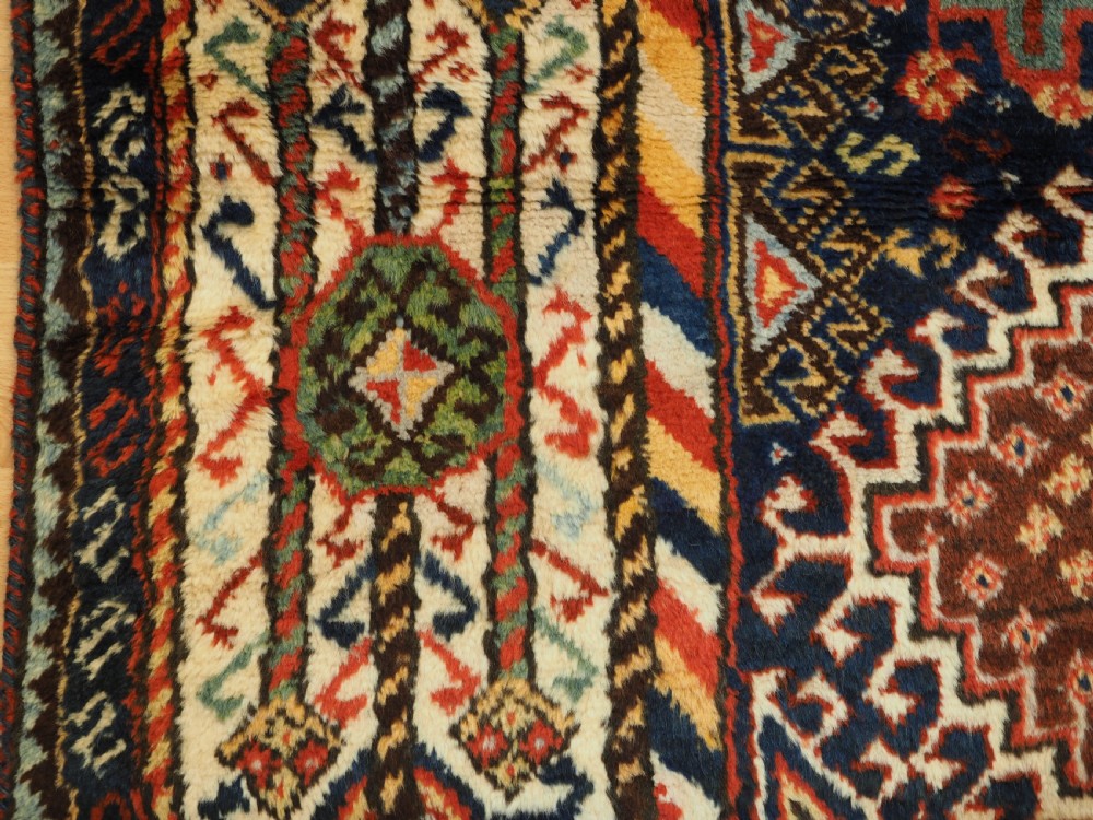 An antique Persian Qashqai Shekarlu wool rug featuring geometric diamond medallions in deep red, navy blue, and cream shades. View XXIV