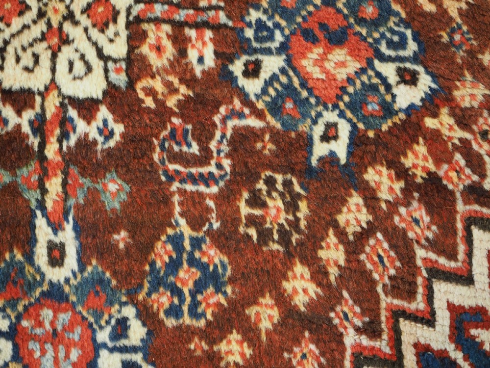 An antique Persian Qashqai Shekarlu wool rug featuring geometric diamond medallions in deep red, navy blue, and cream shades. View XXV