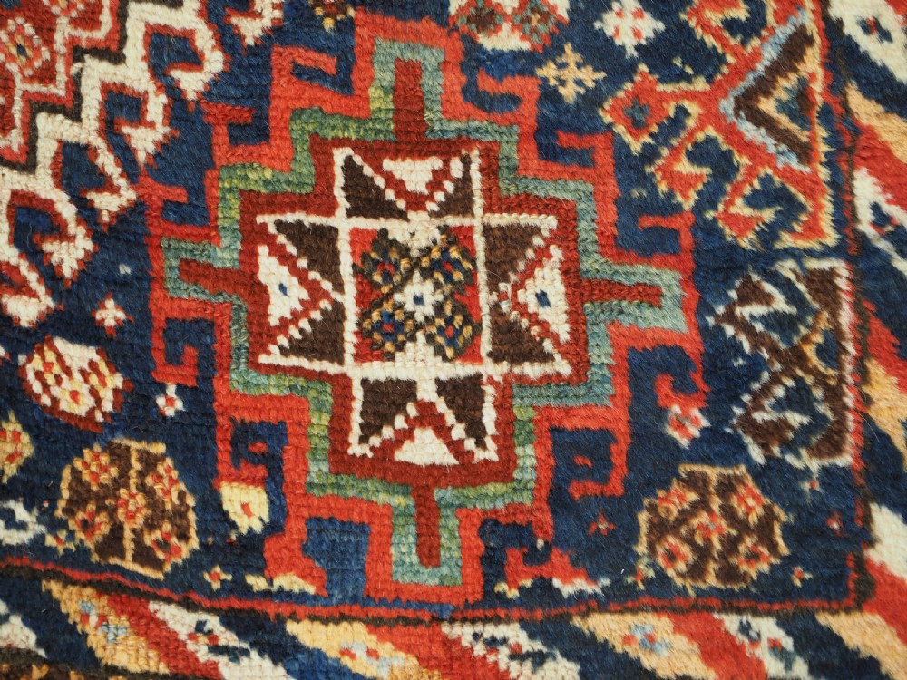 An antique Persian Qashqai Shekarlu wool rug featuring geometric diamond medallions in deep red, navy blue, and cream shades. View XXVI