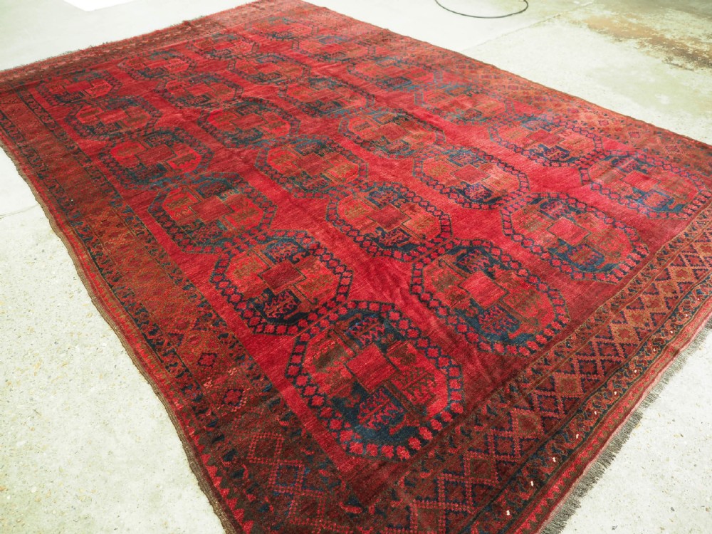 A large hand-knotted wool Afghan carpet featuring a deep red field patterned with repeating dark blue octagonal gul motifs and a geometric border. View II