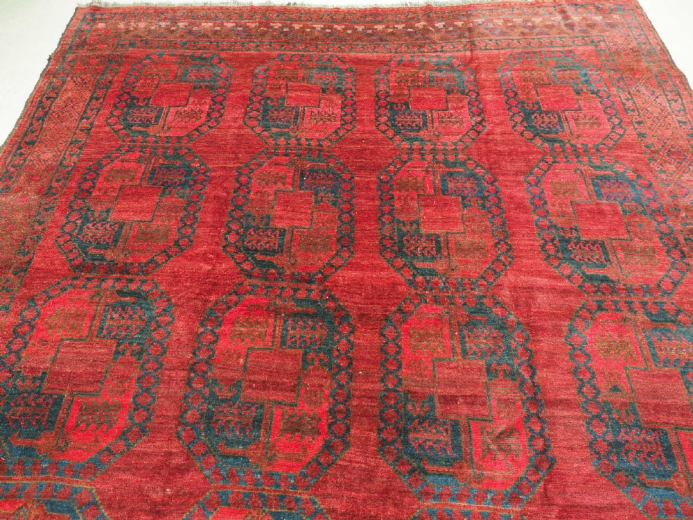 A large hand-knotted wool Afghan carpet featuring a deep red field patterned with repeating dark blue octagonal gul motifs and a geometric border. View III