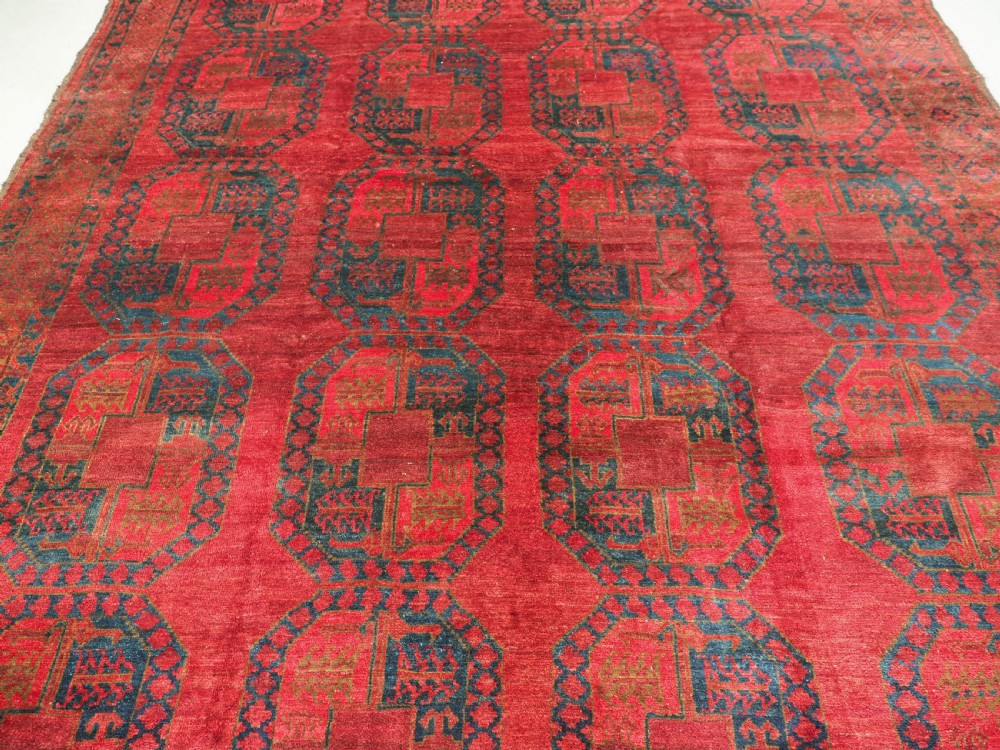 A large hand-knotted wool Afghan carpet featuring a deep red field patterned with repeating dark blue octagonal gul motifs and a geometric border. View IV