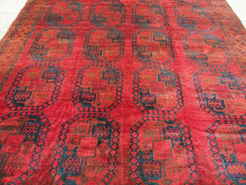 A large hand-knotted wool Afghan carpet featuring a deep red field patterned with repeating dark blue octagonal gul motifs and a geometric border. View V