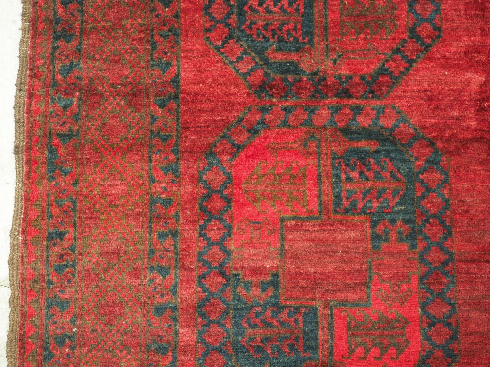 A large hand-knotted wool Afghan carpet featuring a deep red field patterned with repeating dark blue octagonal gul motifs and a geometric border. View VIII