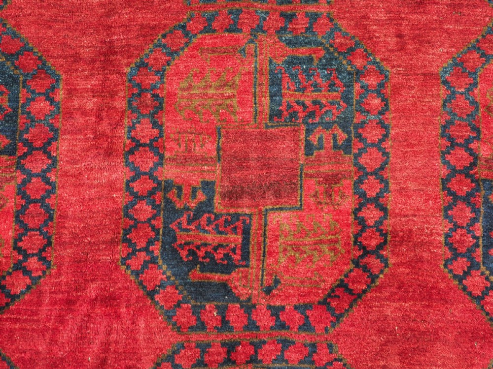 A large hand-knotted wool Afghan carpet featuring a deep red field patterned with repeating dark blue octagonal gul motifs and a geometric border. View XI
