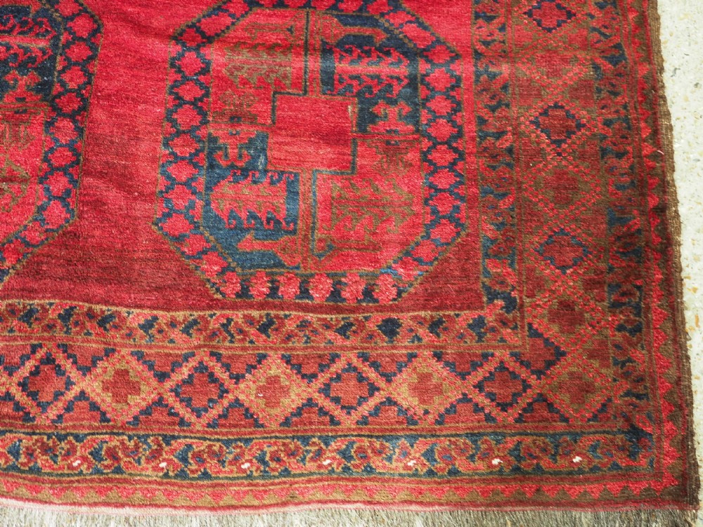 A large hand-knotted wool Afghan carpet featuring a deep red field patterned with repeating dark blue octagonal gul motifs and a geometric border. View XII