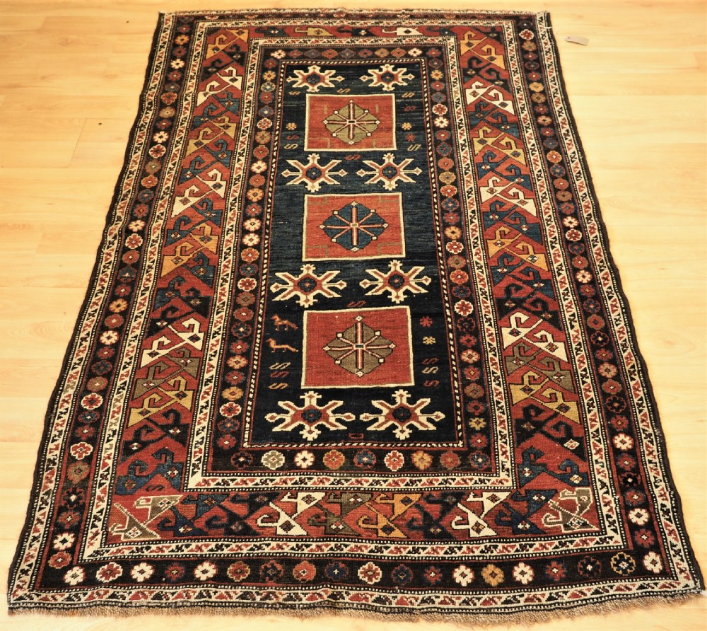 An antique Caucasian Karagashli rug featuring three central square medallions within a dark blue field and geometric borders.