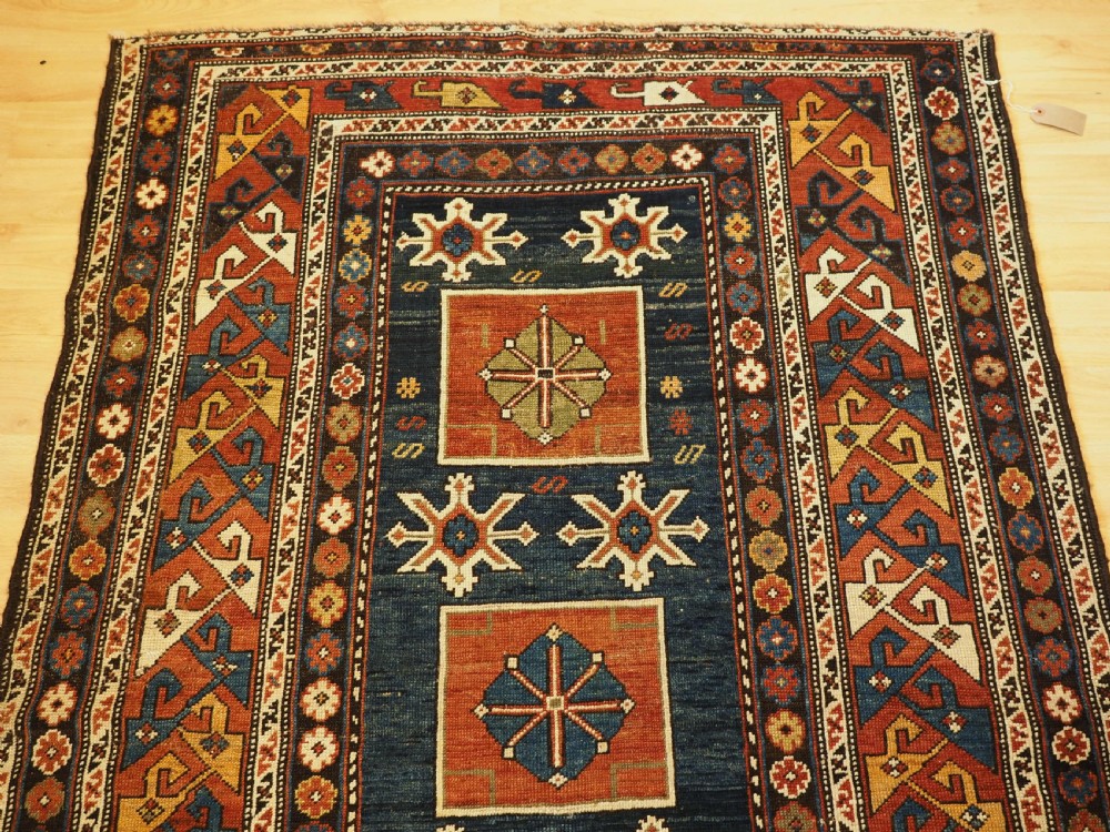 An antique Caucasian Karagashli rug featuring three central square medallions within a dark blue field and geometric borders. View II