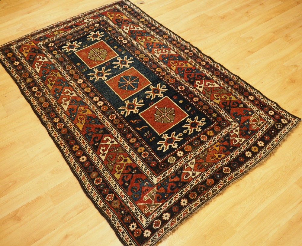 An antique Caucasian Karagashli rug featuring three central square medallions within a dark blue field and geometric borders. View III