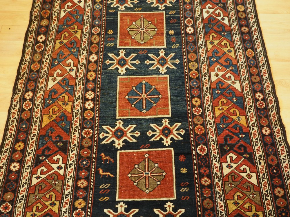 An antique Caucasian Karagashli rug featuring three central square medallions within a dark blue field and geometric borders. View IV