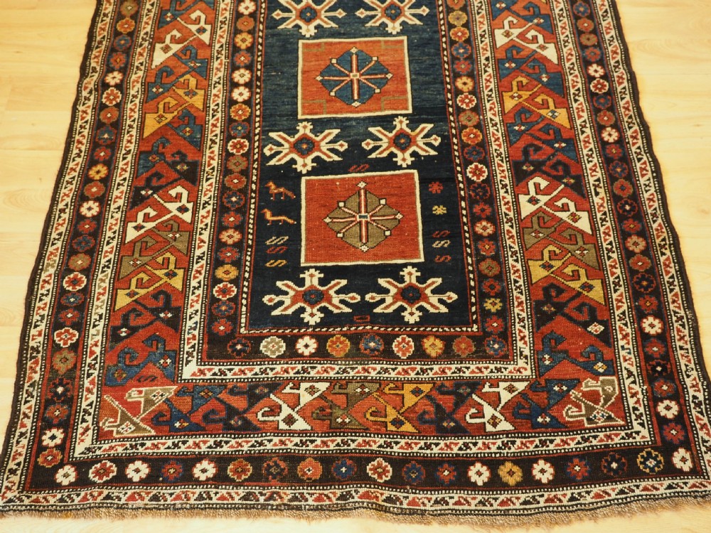 An antique Caucasian Karagashli rug featuring three central square medallions within a dark blue field and geometric borders. View V