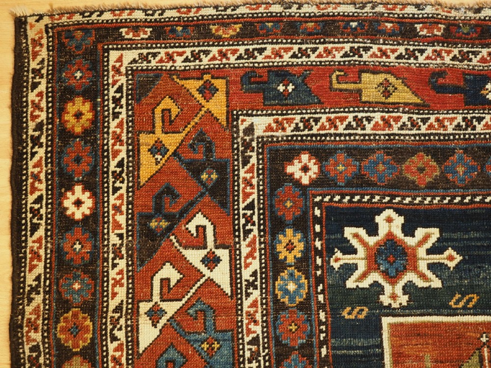 An antique Caucasian Karagashli rug featuring three central square medallions within a dark blue field and geometric borders. View VI