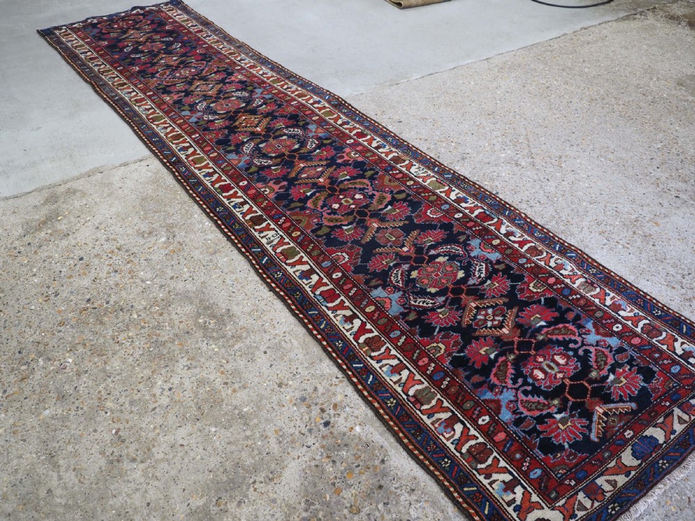 An antique long hand-knotted Persian Hamadan runner rug featuring geometric medallions in shades of dark blue, red, cream, and terracotta. View II