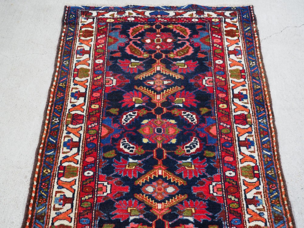 An antique long hand-knotted Persian Hamadan runner rug featuring geometric medallions in shades of dark blue, red, cream, and terracotta. View III