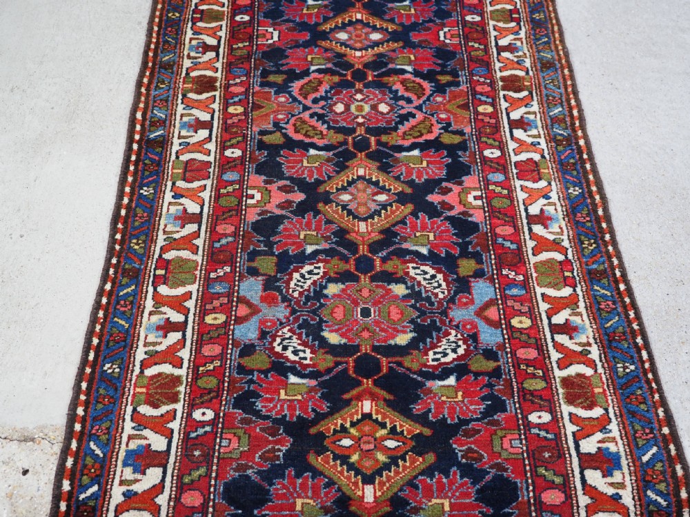 An antique long hand-knotted Persian Hamadan runner rug featuring geometric medallions in shades of dark blue, red, cream, and terracotta. View IV