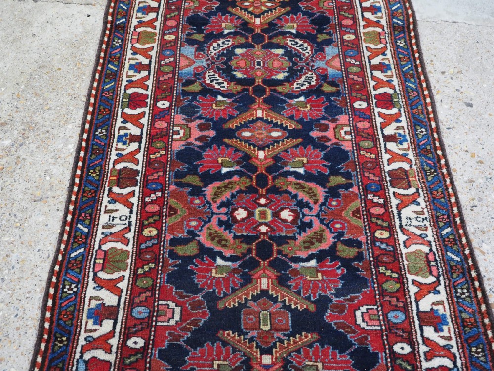 An antique long hand-knotted Persian Hamadan runner rug featuring geometric medallions in shades of dark blue, red, cream, and terracotta. View V
